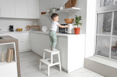 Küçük çocuk mutfakta mikrodalga fırının yanındaki merdivende. Tehlikedeki çocuk