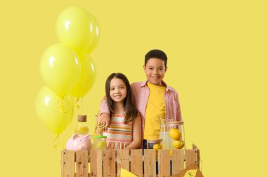 Sevimli küçük çocuklar sarı arka planda limonata standında sarılıyorlar.