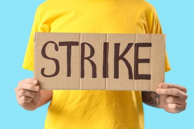 Mavi arka planda kelime STRIKE ile pankart tutan genç adam protesto, yakın plan