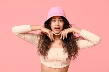 Pembe arka planda şapkalı, şık giyinen Afro-Amerikan bir kadın.