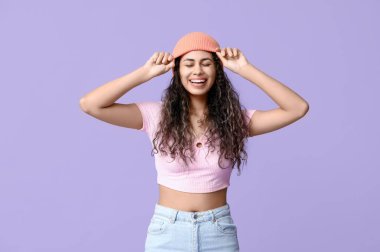 Havalı Afro-Amerikalı kadın üstümde kot pantolon ve eflatun arka planda şapka