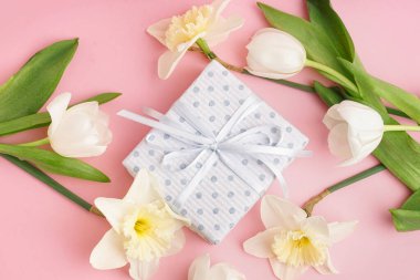Pembe arka planda güzel laleler ve nergis çiçekleri olan hediye kutusu.
