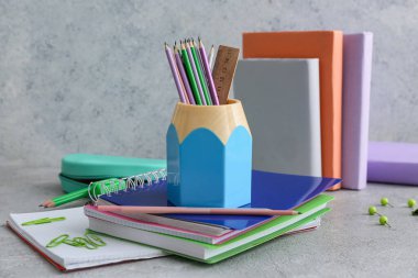 Gri arkaplana karşı masadaki kalem tutucu ve defterler
