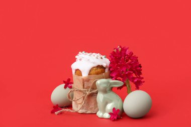 Paskalya pastasının güzel kompozisyonu, kırmızı arka planda boyanmış yumurtalar, sümbül ve tavşan.