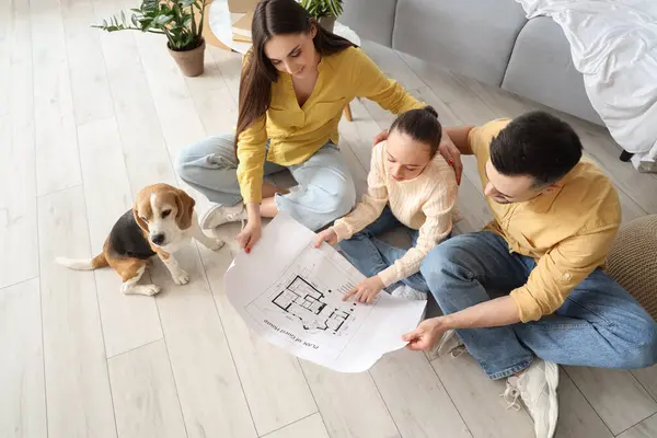Happy family with house plan and Beagle dog in room on moving day