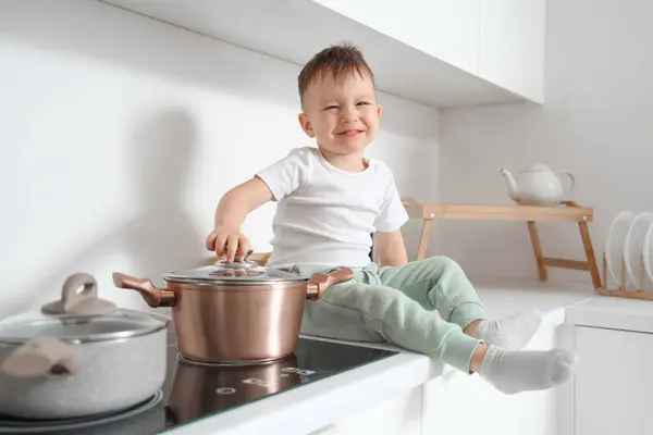 Little boy opening lid pot on electric stove in kitchen. Child at risk