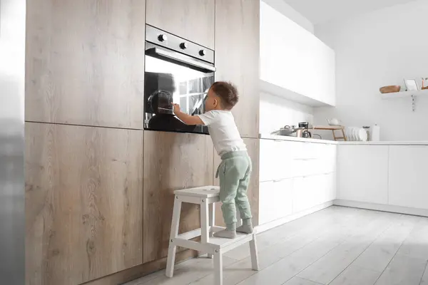 Little boy climbing on step stool near oven in kitchen. Child at risk