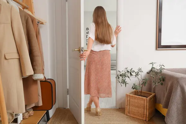 Young woman walking away through open door at home, back view
