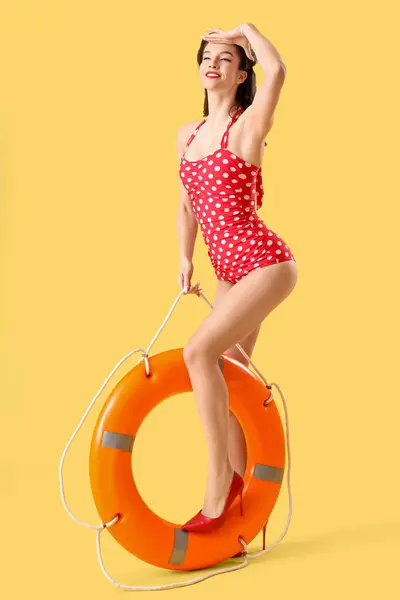 Beautiful pin-up lifeguard with ring buoy on yellow background