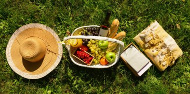 Parktaki çimlerde romantik piknik için ekose, şapka ve sepet lezzetli yiyecek ve içecekler.