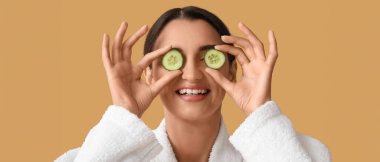 Bornozlu ve bej arka planda salatalık dilimleri olan genç bir kadın.