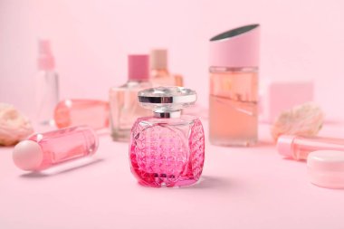 Bir şişe parfüm ve pembe arka planda farklı kozmetik ürünleri.