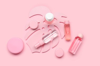Farklı kozmetik ürünleri ve pembe arka planda dekoratif palmiye yaprağı içeren kompozisyon