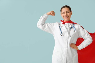 Süper kahraman kostümlü güzel bayan doktor mavi arka planda kaslarını gösteriyor.