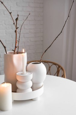 Yakıcı mumlar ve vazolar, hafif tuğla duvarın yanındaki masada bitki dalları, yakın plan.