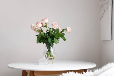 Işık duvarının yanındaki masada güzel gül çiçekleri olan vazo