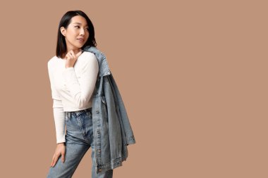 Kahverengi arka planda şık kot elbiseli güzel bir Asyalı kadın.