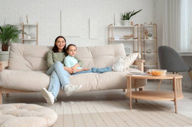Mutlu anne ve küçük kızı evdeki kanepede televizyon izliyorlar.