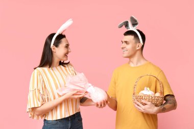 Paskalya sepeti, tavşan kulakları ve pembe arka planda hediyeleri olan mutlu genç çift.