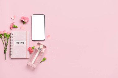Modern cep telefonlu kompozisyon, bir şişe parfüm ve pembe arka planda karanfil çiçekleri.
