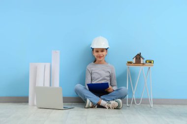 Mavi duvarın yanında dizüstü bilgisayarı olan küçük bir mimar oturuyor.