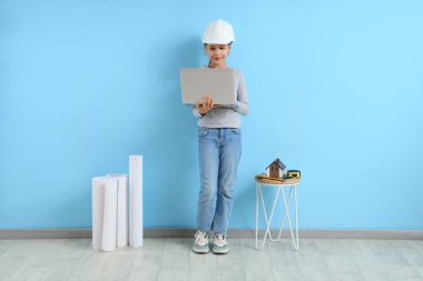 Mavi duvarın yanında dizüstü bilgisayar kullanan küçük mimar.