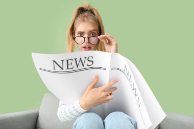 Yeşil duvarın yanındaki kanepede gazete okuyan duygusal genç kadın.