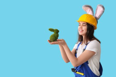 Mavi arka planda Paskalya tavşanı olan tavşan kulaklı kadın işçi.