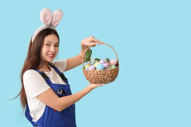 Mavi arka planda Paskalya yumurtaları olan tavşan kulaklı Asyalı kadın işçi.