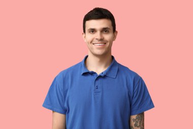 Pembe arka planda şık mavi tişörtlü yakışıklı genç adam, yakın plan.