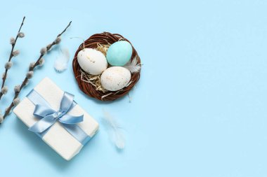 Yuvada boyanmış Paskalya yumurtaları ve mavi arka planda hediye kutusu.