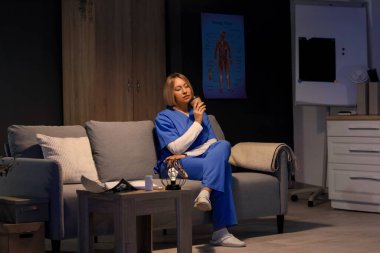 Akşamları hastanedeki kanepede oturan kahve fincanlı kadın hemşire.