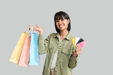 Gri arka planda kredi kartları ve alışveriş çantaları olan güzel genç bir kadın.