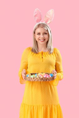 Pembe arka planda Paskalya yumurtaları olan tavşan kulaklı güzel bir kadın.