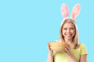 Mavi arka planda Paskalya yumurtaları olan tavşan kulaklı güzel bir kadın.