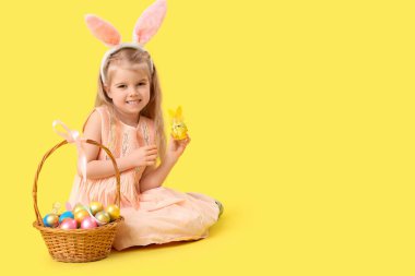 Tavşan kulaklı küçük kız Paskalya yumurtaları sarı arka planda oturuyor.