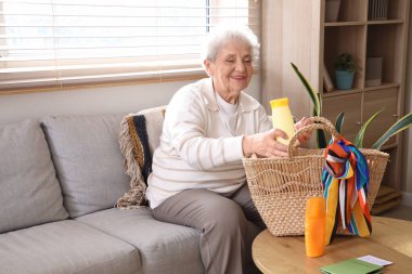 Kıdemli bayan turist evdeki plaj çantasına güneş kremi koyuyor.