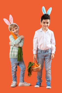 Turuncu arka planda oyuncak havuçları olan tavşan kulaklı şirin çocuklar. Paskalya kutlaması