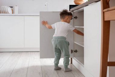 Küçük çocuk mutfakta çekmece açıyor. Tehlikedeki çocuk