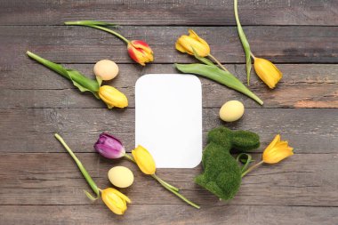 Oyuncak tavşanlı boş kart, tahta arka planda Paskalya yumurtası ve laleler.