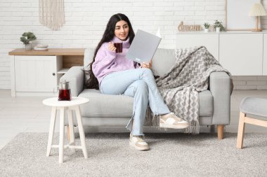 Evdeki kanepede bir bardak sıcak çay ve dergi ile güzel genç bir kadın.