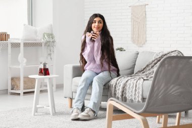 Evdeki kanepede bir fincan sıcak çay içen güzel genç bir kadın.