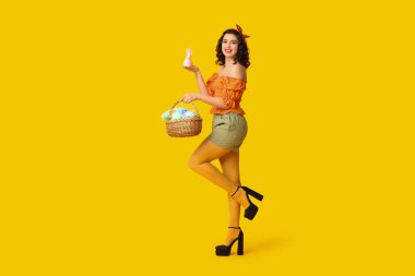 Paskalya sepeti ve sarı arka planda tavşanı olan güzel bir kadın.