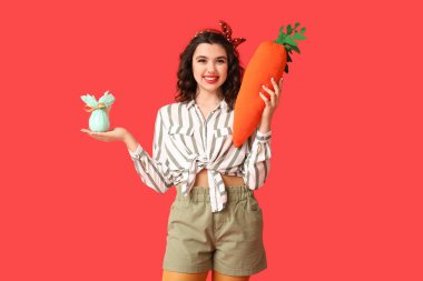 Paskalya yumurtası ve kırmızı arka planda oyuncak havuç tutan güzel bir kadın.