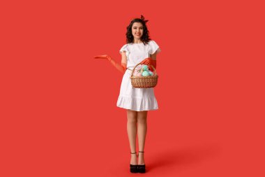 Paskalya sepeti tutan güzel bir kadın ve kırmızı arka planda bir şey gösteriyor.