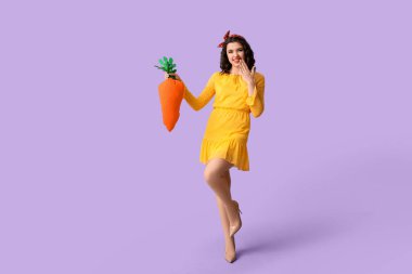 Leylak arka planında oyuncak havuç tutan duygusal kadın.