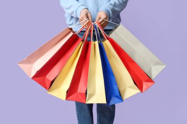 Leylak arka planında bir sürü alışveriş çantası olan genç bir kadın.