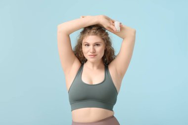 Mavi arka planda deodorantı olan güzel genç bir kadın.