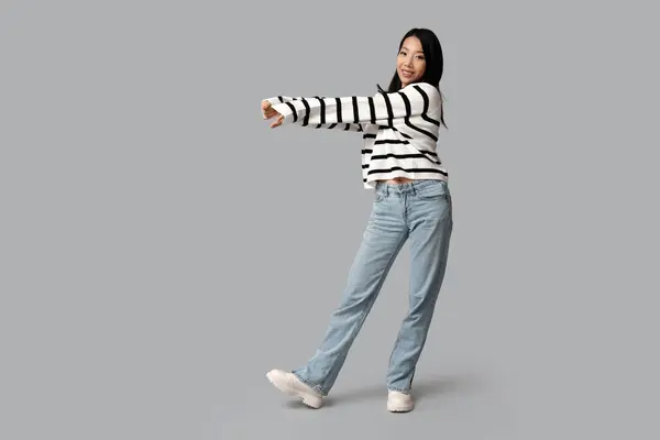 美しい若い幸せなアジアの女性 スタイリッシュなジーンズで灰色の背景 — ストック写真