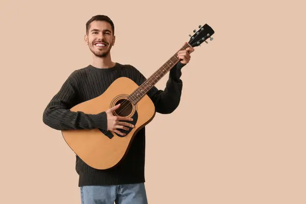 stock image Handsome young man playing guitar on beige background